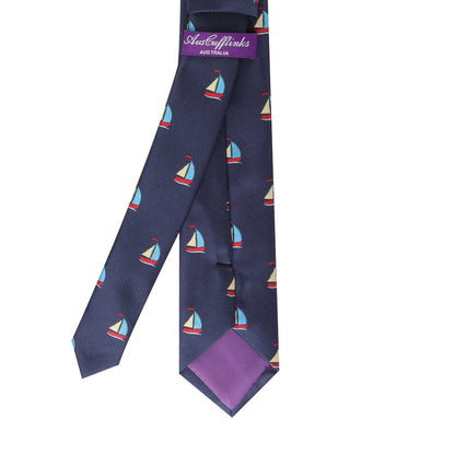 The Nautical Skinny Tie features a navy-blue background adorned with a pattern of small red, white, and blue sailboats. Its purple lining and "AussieCufflinks Australia" label add to its distinguished flair, making it perfect for anyone looking to set sail in nautical style.