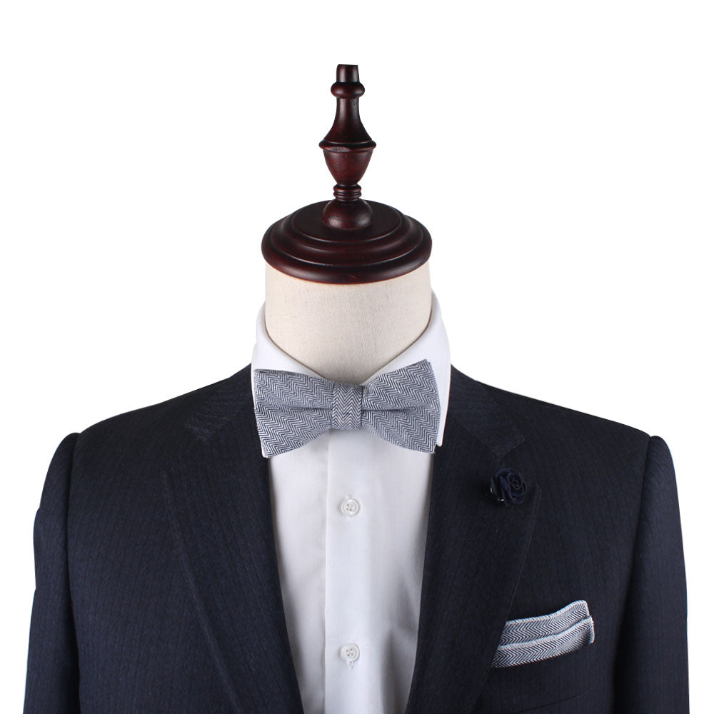 A mannequin dressed in a navy suit jacket with a white shirt, gray bow tie, and a matching Navy Blue Herringbone Pocket Square exudes elegance.