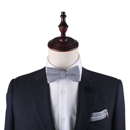 Mannequin dressed in a dark suit, white shirt, Navy Blue Herringbone Bow Tie, and pocket square, with a paisley floral lapel pin.