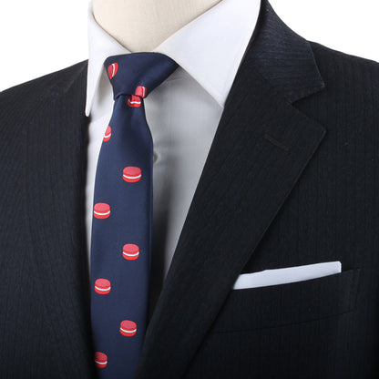 A mannequin exudes sophistication in a black pinstripe suit with a white shirt, highlighted by the Macaron Skinny Tie. The red and white gourmet dessert patterns on the tie add a playful twist for dessert lovers.