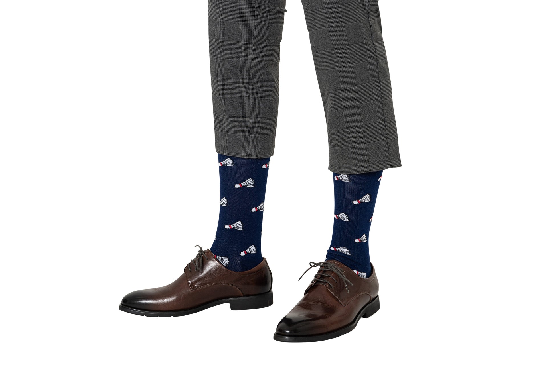 A person stands against a white background wearing gray plaid pants, brown leather dress shoes, and navy blue Badminton Socks featuring a shuttlecock print and moisture-wicking fabric.