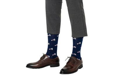 A person stands against a white background wearing gray plaid pants, brown leather dress shoes, and navy blue Badminton Socks featuring a shuttlecock print and moisture-wicking fabric.