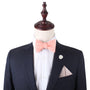 A mannequin styled in a dark suit with a white shirt, a vibrant Pink Orange Self Tie Bow Tie, a matching pocket square, and a white lapel pin.