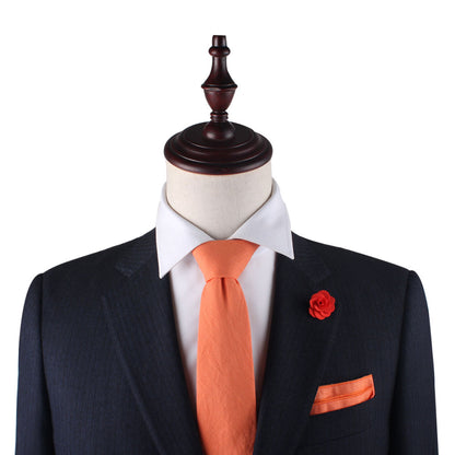 A mannequin showcases sleek sophistication with a suit featuring sunny hues: a white shirt, Peach Orange Cotton Skinny Tie & Pocket Square Set, and matching lapel flower.