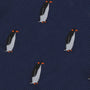 Close-up of a dark blue fabric with an embroidered pattern of penguins with orange beaks and feet, evenly spaced throughout the Penguin Bow Tie, exuding a cold elegance that contrasts beautifully with its charming design.