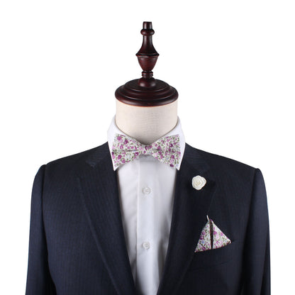 A mannequin dressed in a dark suit with a white shirt, accentuated by the Pink Roses Floral Cotton Bow Tie & Pocket Square Set, featuring elegant pink roses.