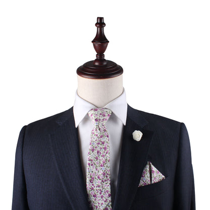 A mannequin in a dark suit with a white shirt is accessorized by the Pink Roses Floral Cotton Skinny Tie and Pocket Square Set, exuding perennial charm against a plain background.