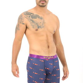A tattooed man stands against a plain white background, wearing Racing Car Brief with blue and red patterns, exuding an unexpected coziness in his relaxed pose.