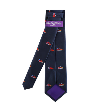 A dark blue necktie featuring a red and blue boat pattern, shown front and back. The back of the tie has a purple label displaying the brand "AUSCUFFLINKS," adding urban flair to its modern style, called the Sneaker Skinny Tie.
