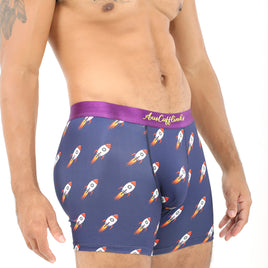 A man wears Rocket Underwear—navy blue, space-themed boxers with rockets and a purple waistband with gold text—standing against a plain white background. This fun gift for space lovers combines comfort and playful style.