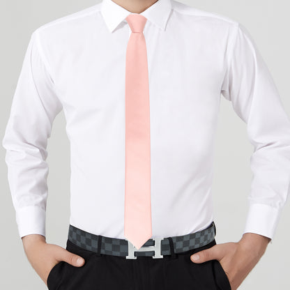 Person exuding modern elegance in a white dress shirt, sleek rose gold skinny necktie paired with a matching pocket square, black pants with a checkered belt, standing confidently with hands in pockets.