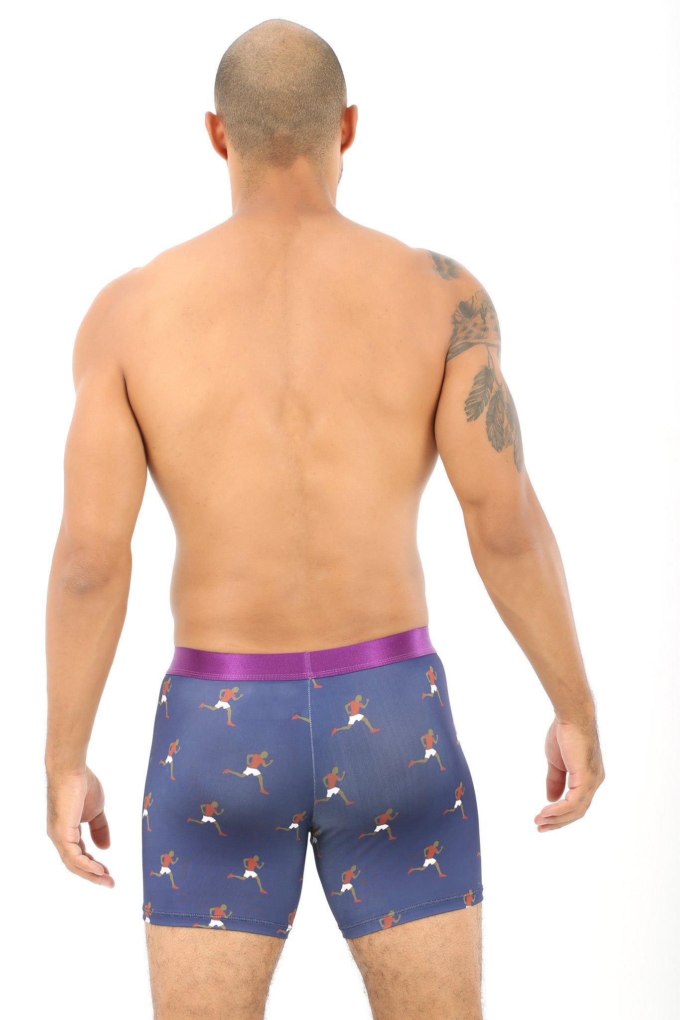 A shirtless person with a tattoo on their arm stands facing away, wearing cozy Athletics Underwear in a dark color with a vibrant pattern reminiscent of crossing the finish line in life's race.