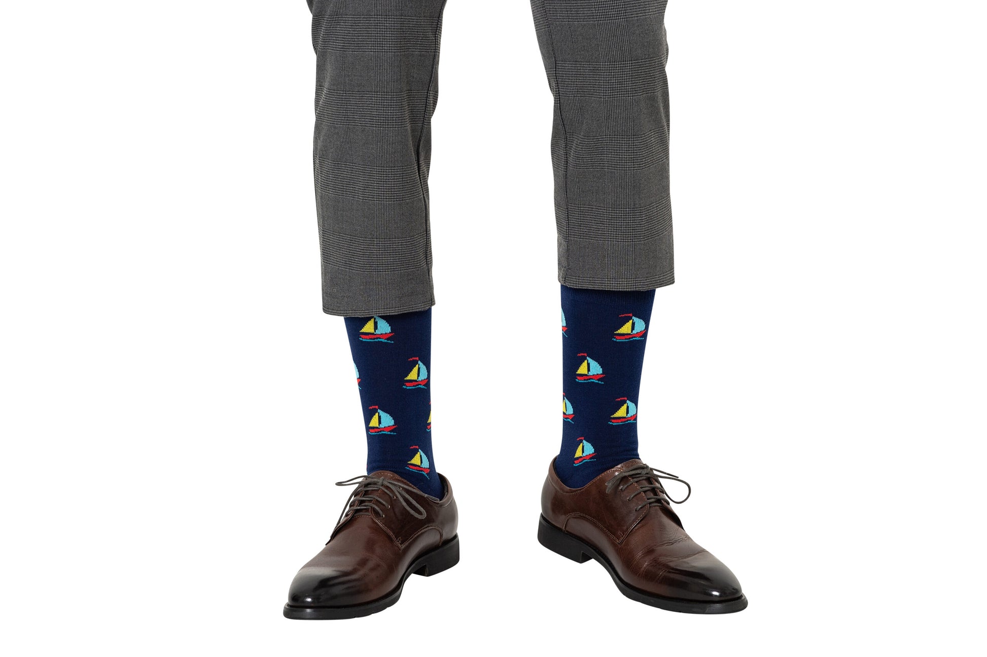 A man wearing gray patterned pants and dark brown dress shoes, showcasing Sail Boat Socks with vibrant sailboat designs in navy blue, perfect for adding a touch of sailing spirit and comfort.