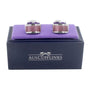 A pair of Sapphire Pink Cufflinks displayed on a purple cushion inside a navy blue box labeled "AUSCufflinks," adding a touch of sophistication.