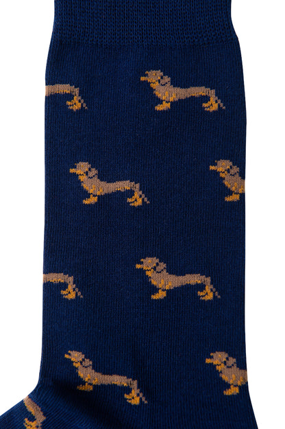 A pair of Sausage Dog Socks featuring a quirky repeating pattern of small, stylized canine figures in yellow and brown on a blue background.