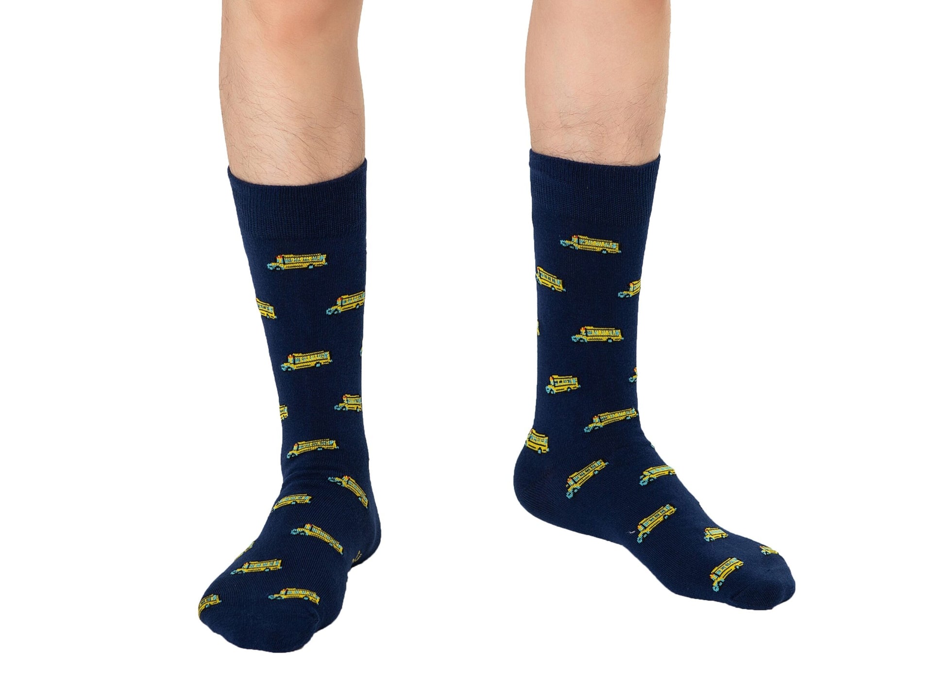 Close-up of a person's legs wearing School Bus Socks adorned with a charming yellow school bus pattern against navy blue fabric, evoking a sense of nostalgia. The person is taking a confident step on a pristine white background.