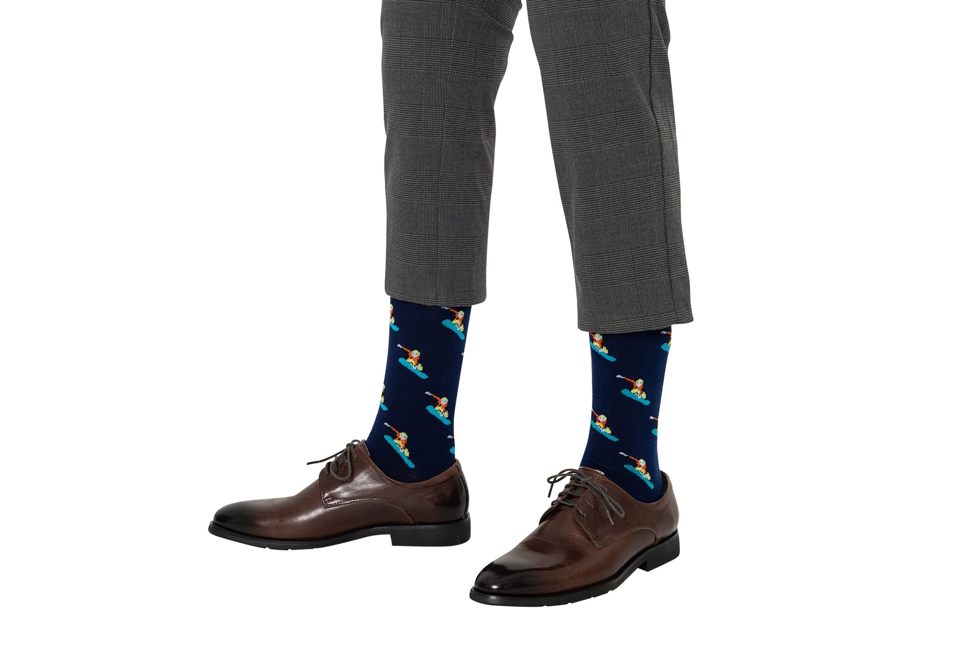 A person is wearing gray plaid pants, brown dress shoes, and Navy Snowboarder Socks featuring moisture-wicking fabric with colorful cartoon skateboarders on a white background.