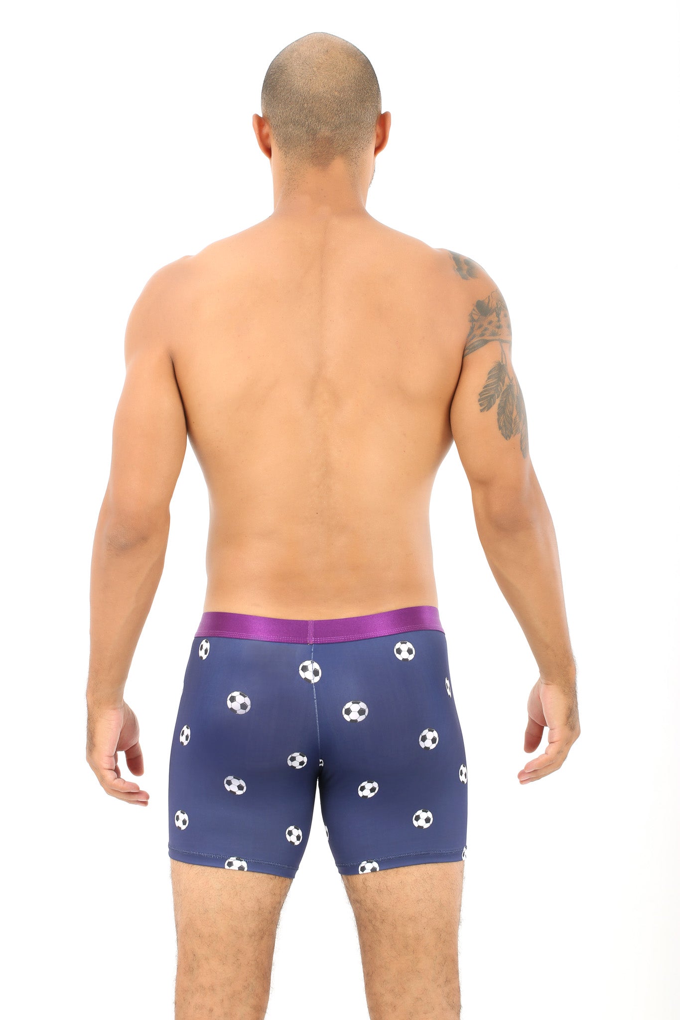 Seen from behind, a person with a tattoo on their left arm exudes comfort in blue Soccer Ball Print Underwear adorned with pretzel patterns and accented by a purple waistband.
