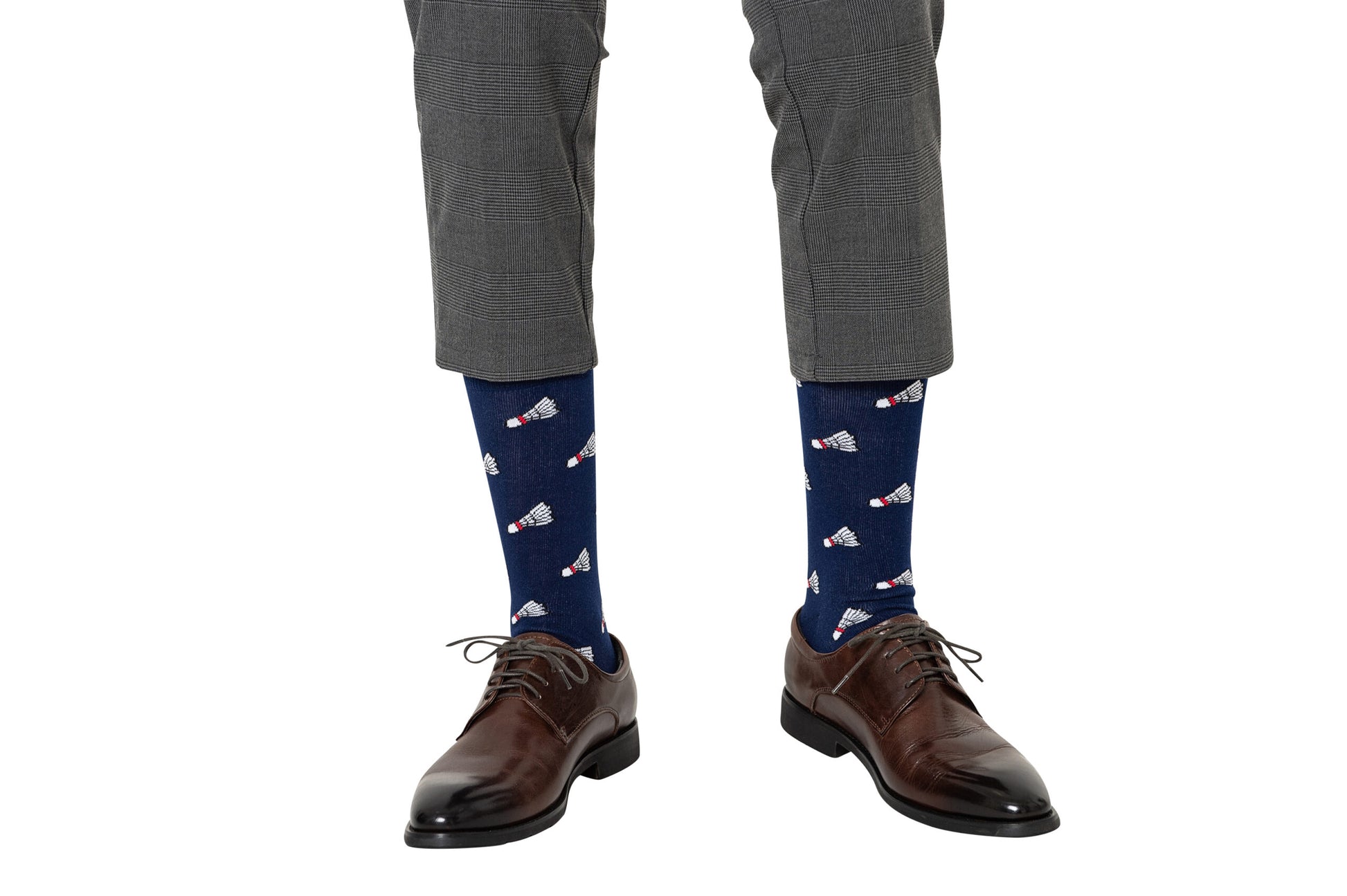 A person stands against a white background wearing gray plaid pants, brown dress shoes, and navy blue Badminton Socks featuring a moisture-wicking shuttlecock print.