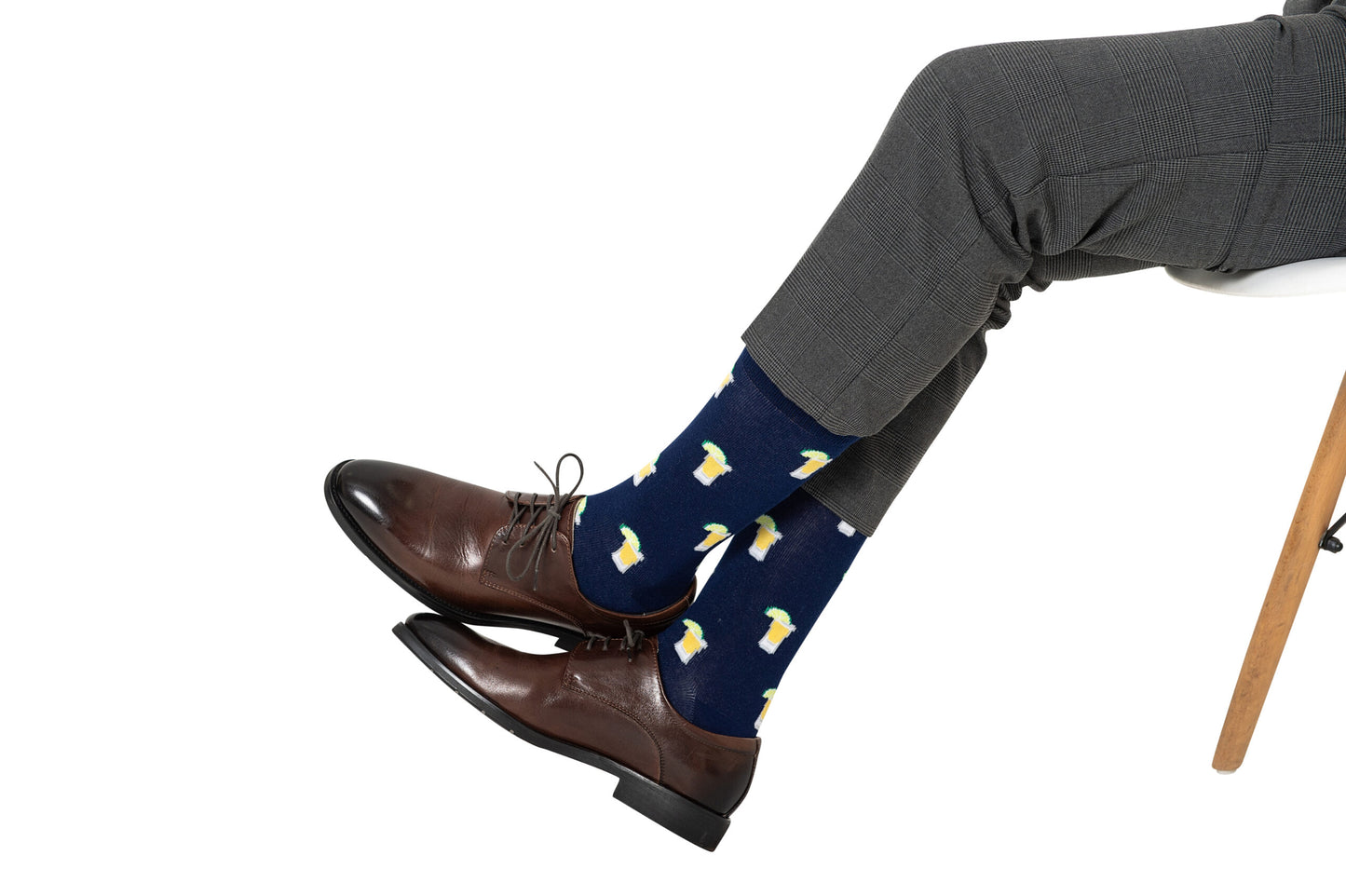 A person wearing gray dress pants, brown dress shoes, and Tequila Socks sits cross-legged on a white chair.