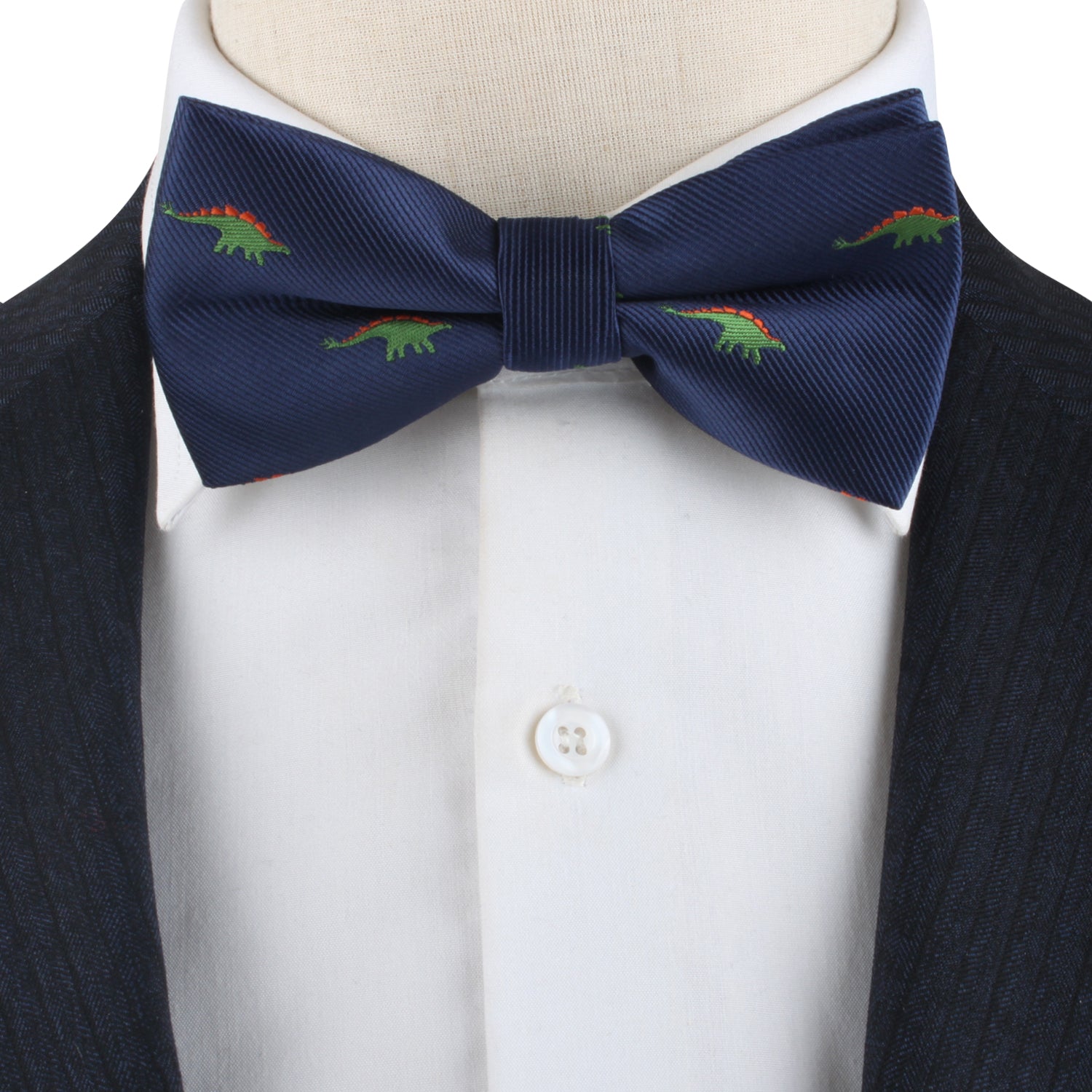 A close-up of the Stegosaurus Bow Tie, featuring a navy blue fabric adorned with small green and red dinosaur patterns, worn with a white button-up shirt and a dark jacket. This accessory adds a touch of prehistoric panache to the ensemble.