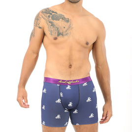 A man with a tattoo on his shoulder stands against a white background, wearing Swimming Boxer in dark blue with a purple waistband and white patterns, exuding the same inviting plushness as a serene pool awaiting a dive.