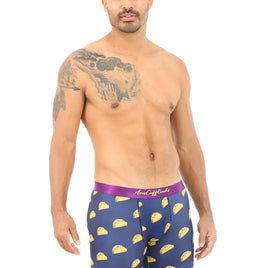 A man wears Taco Underwear featuring purple fabric with yellow taco designs, ideal for taco enthusiasts, and displays a tattoo on his left shoulder and arm.