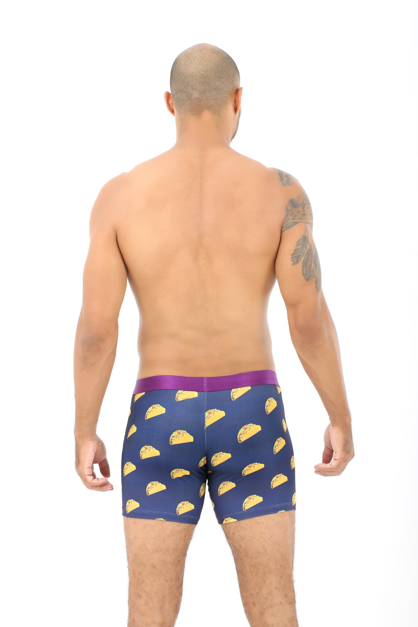 A man with a shaved head is seen from behind wearing navy Taco Underwear, featuring a taco print and purple waistband. Ideal for taco lovers, these moisture-wicking boxer briefs ensure comfort stays as fresh as your favorite meal.