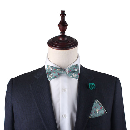 Mannequin dressed in a dark suit and white shirt, highlighted by a floral bow tie and the Teal Floral Pocket Square, complemented with a teal flower lapel pin.