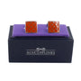 A pair of tear drop orange cufflinks with intricate pattern details adds a splash of color to your formal attire. Displayed on a purple cushion above a black box labeled "AUSCUFFLINKS," these cufflinks are perfect for making a stylish statement.