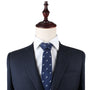 A mannequin dressed in a dark pinstripe suit, white dress shirt, and the Tennis Slim Tie featuring a small repeating pattern exudes timeless refinement.