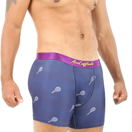 A man wears Tennis Underwear, featuring blue boxer briefs with tennis racket designs and a purple waistband embroidered with gold text for ultimate comfort. A tattoo on his upper chest and shoulder adds an ace touch to his look.