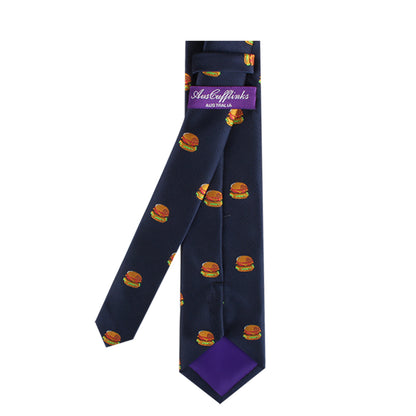 The Burger Skinny Tie, featuring a bold navy blue hue and an eye-catching pattern of small hamburger images, is a stylish statement piece. It includes a purple label with striking white text.