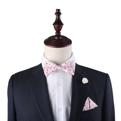 A mannequin is outfitted in a black suit with a white shirt, a Tonal Pink Azalea Floral Bow Tie, a matching pocket square, and a white flower lapel pin.