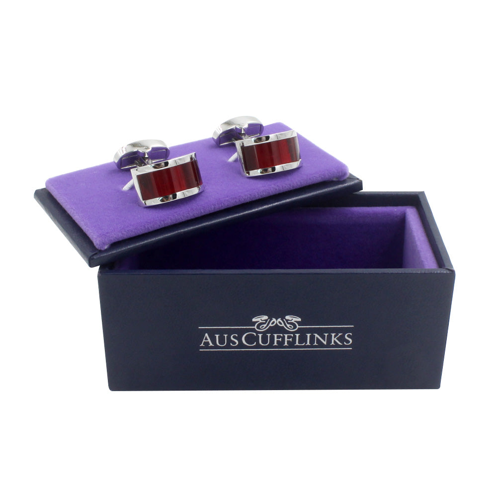 A pair of Ruby Stone Red Cufflinks with a red and silver design displayed in an open black box with a purple interior, exuding gem-like brilliance. The box lid reads "AUSCUFFLINKS", perfect for the discerning gentleman.