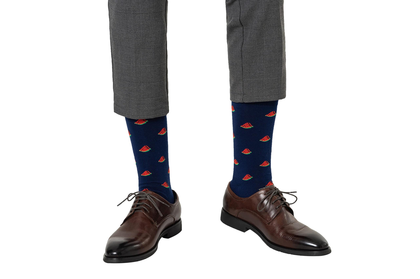 Person joyfully stepping in gray plaid pants, Watermelon Socks, and brown leather dress shoes.
