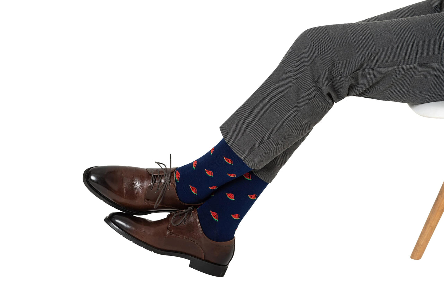 A person in gray trousers and brown leather shoes, with ankles crossed, is taking a step in Watermelon Socks.