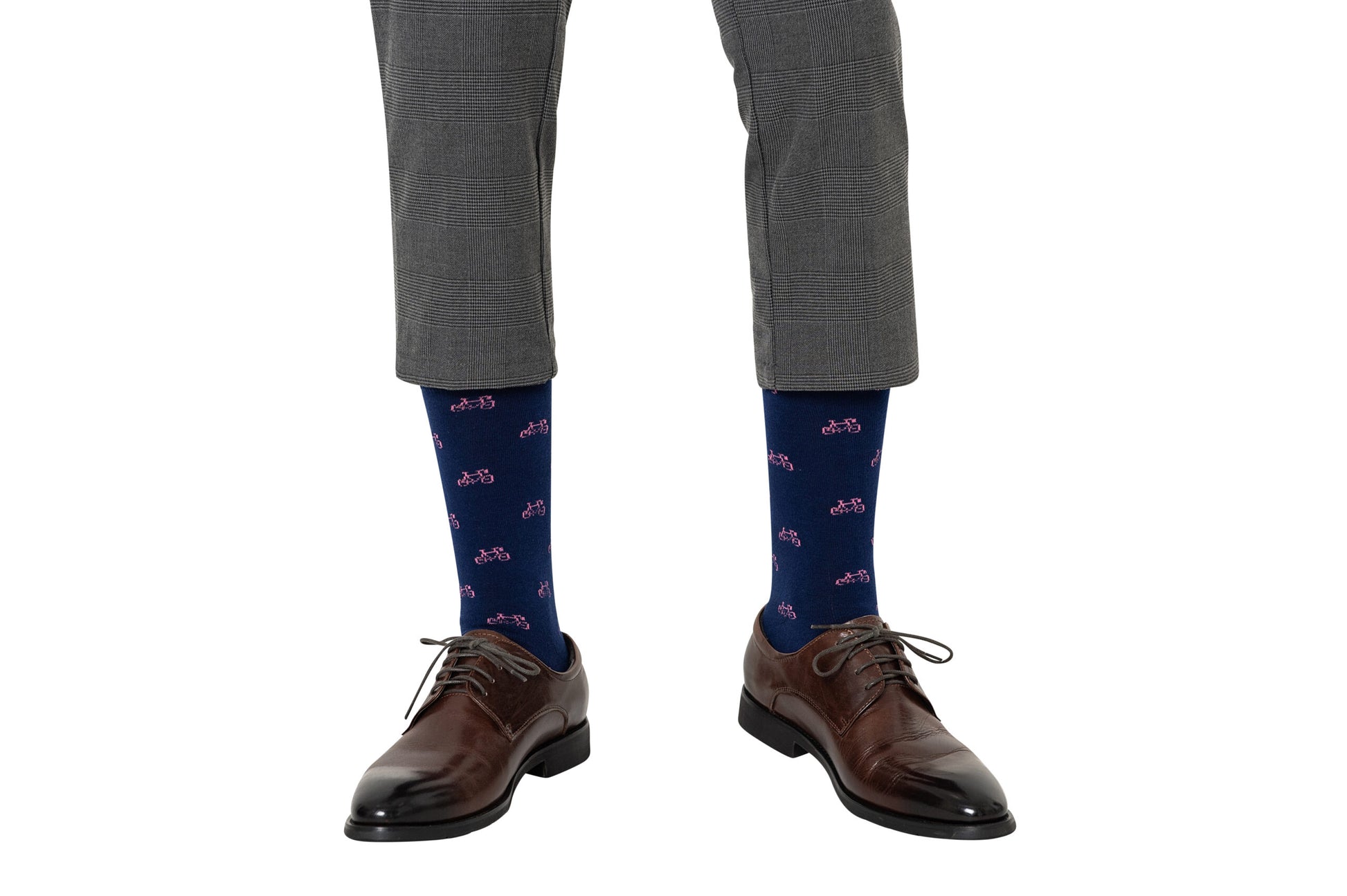 A person wearing grey plaid pants, Pink Bike Socks for a touch of whimsy, and brown leather shoes steps confidently, embracing both style and comfort with every pedal.