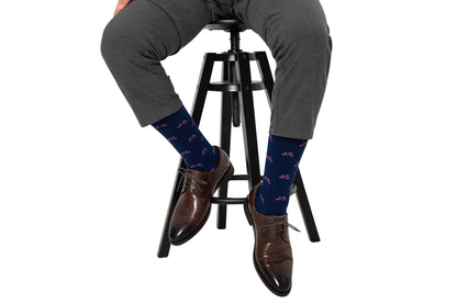 A person is sitting comfortably on a stool, sporting gray pants, brown shoes, and pink socks adorned with bicycle patterns—a nod to pedal enthusiasts who appreciate both style and comfort.